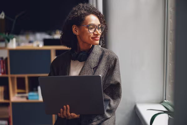 Woman that smile looking at a window, with her laptop in her hand